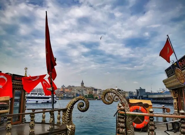 View of Galata Tower and Istanbul skyline from ornate boat deck with Turkish flags and decorative railings on the Golden Horn