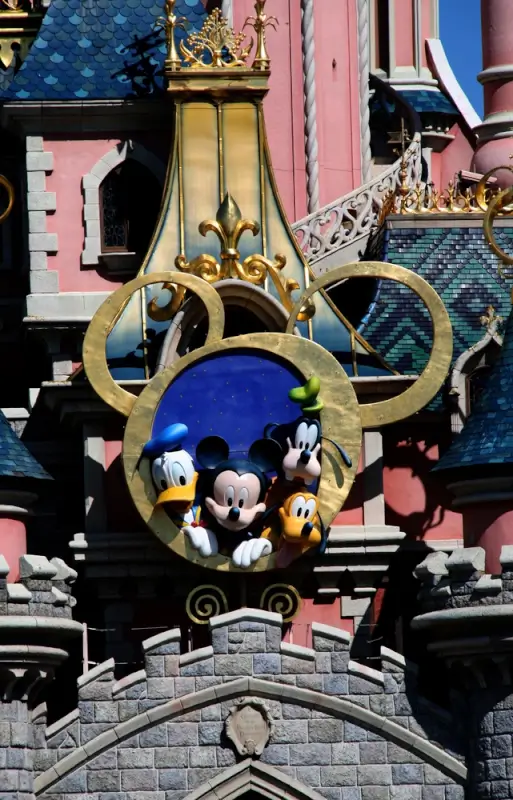 Mickey Mouse, Donald Duck, Goofy and Pluto Disney characters displayed in ornate golden crown decoration on colorful Disneyland castle architecture