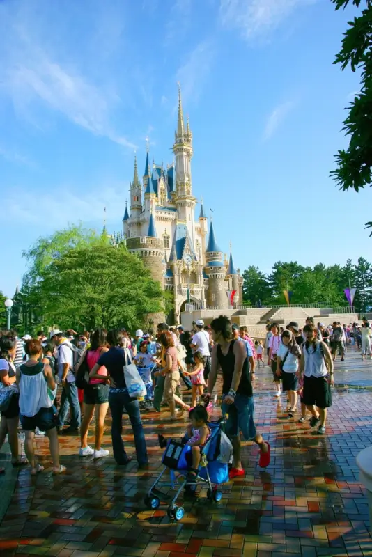 Families with strollers and elderly visitors walking toward iconic Disney castle on sunny day at Disneyland theme park