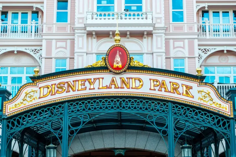 Disneyland Park entrance sign with ornate golden lettering and castle logo above Victorian-style architecture