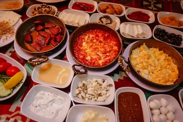 Traditional Turkish breakfast spread with menemen, sucuk, cheese, olives, jams, and honey served on ornate plates and kilim rug