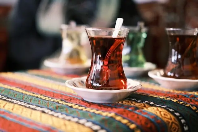 Turkish tea served in traditional tulip-shaped glasses on colorful textile with breakfast setting in background