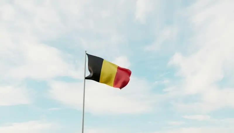 Belgian flag with black, yellow, and red stripes waving against a cloudy blue sky