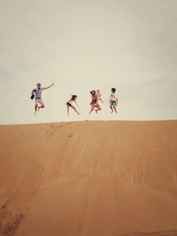 Family of four jumping together on sand dunes during budget-friendly vacation, showing affordable family travel activities