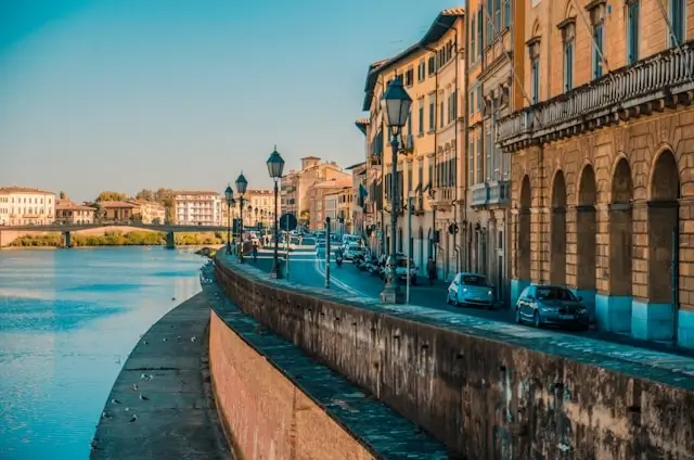 Historic buildings along River Arno waterfront in Pisa with bridge and colorful architecture during sunset