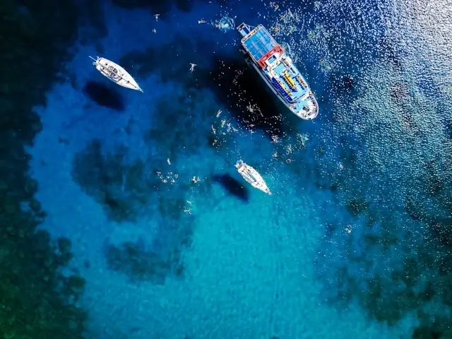 Aerial view of luxury cruise ship and smaller boats in crystal clear turquoise ocean waters during tropical vacation