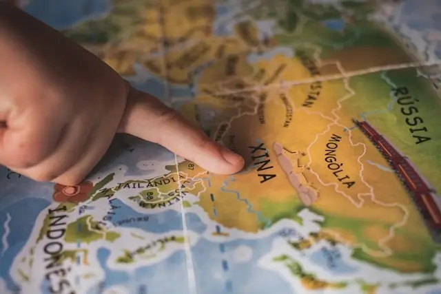 Hand pointing at world map showing destination planning for affordable family travel and choosing budget-friendly locations