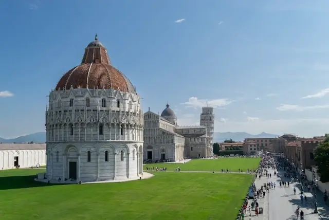 Pisa Baptistery with distinctive dome in Piazza dei Miracoli showing tourists on green lawn