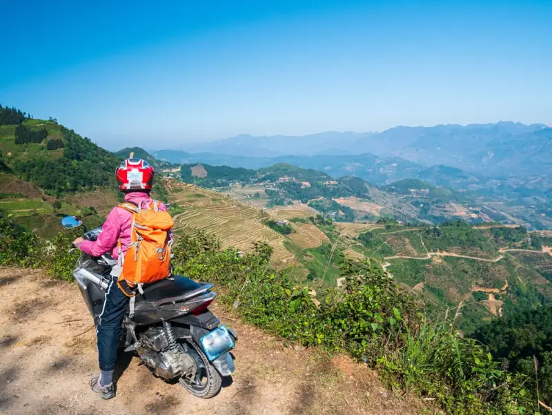 Motorbike rider with backpack overlooking terraced rice fields on Ha Giang Loop mountain road in Vietnam
