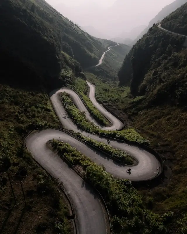 Dramatic hairpin turns on Ma Pi Leng Pass Ha Giang Loop with motorbike navigating winding mountain road through misty valley