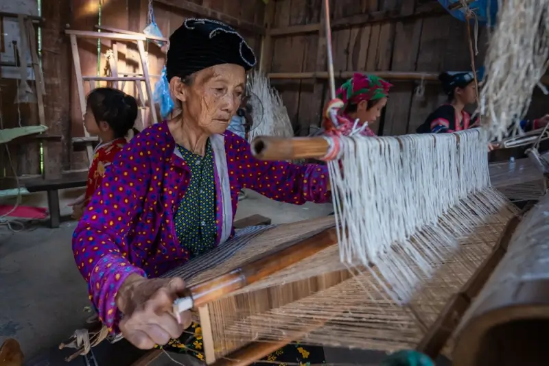 Hmong woman weaving traditional colorful textiles on wooden loom in Lung Tam village along Ha Giang Loop Vietnam