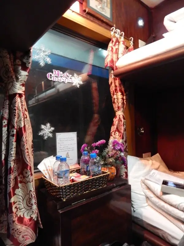 Private sleeper berth on comfortable bus from Hanoi to Lao Cai showing curtains, bedding, and included water for 6-hour overnight journey