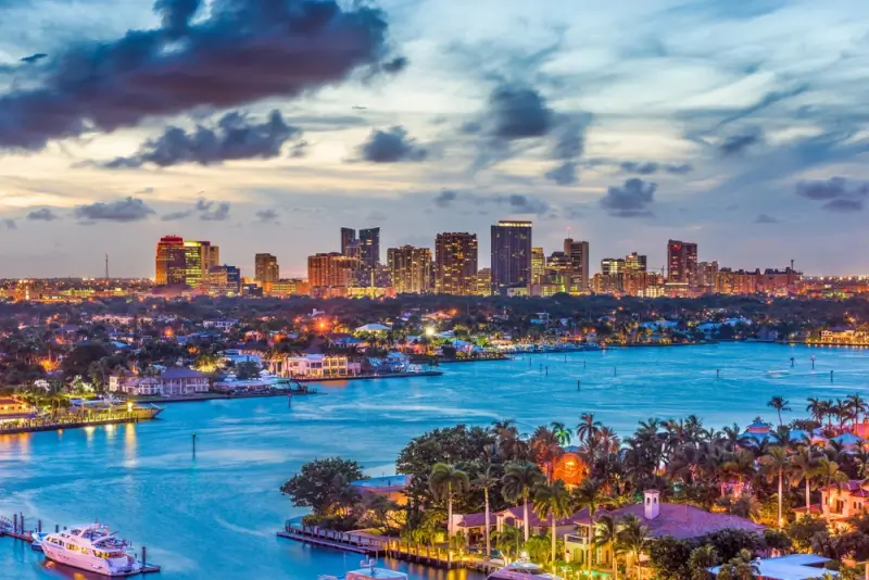Aerial view of dinner cruise ships on coastal waterways with illuminated Fort Lauderdale skyline at dusk in Florida