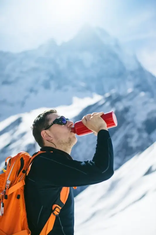 Male hiker drinking from insulated water bottle for outdoor adventure in snowy mountain terrain