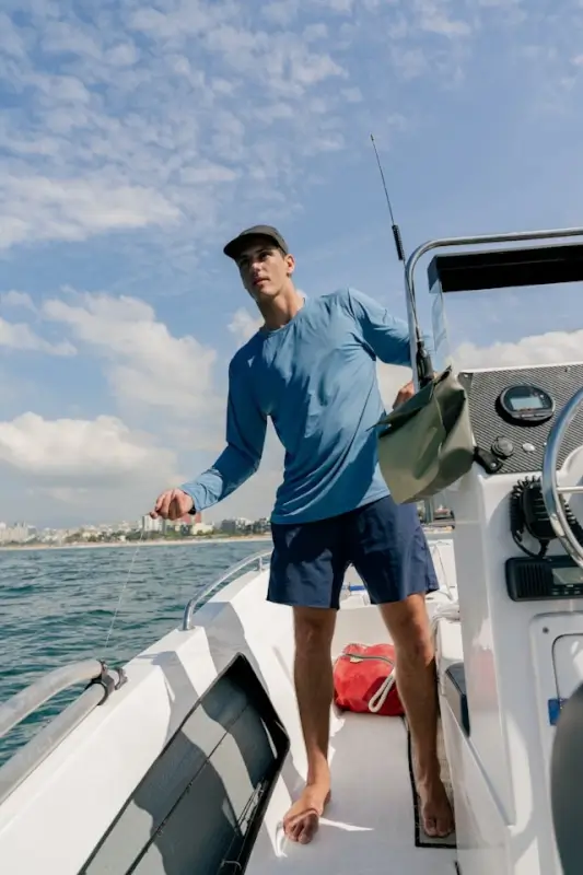 Man wearing custom boat shirts in blue long-sleeve performance fabric while fishing on deck under sunny skies