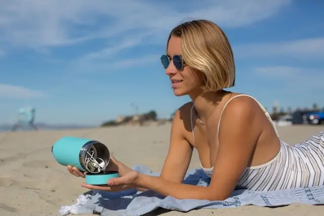 Woman storing electronics in waterproof tumbler while relaxing on sunny beach