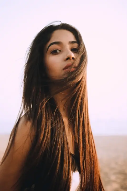 Young woman with smooth youthful skin and long flowing hair against soft pink sky
