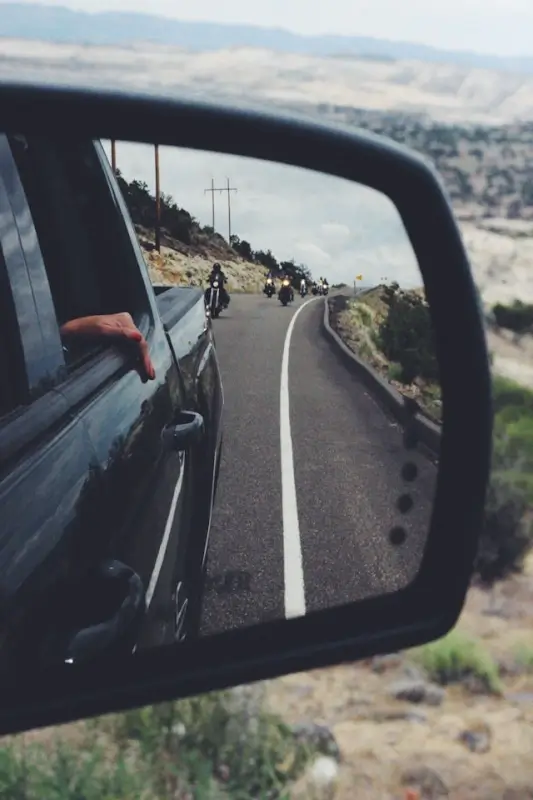 Rear view mirror showing motorcyclists on scenic mountain road during adventurous road trip