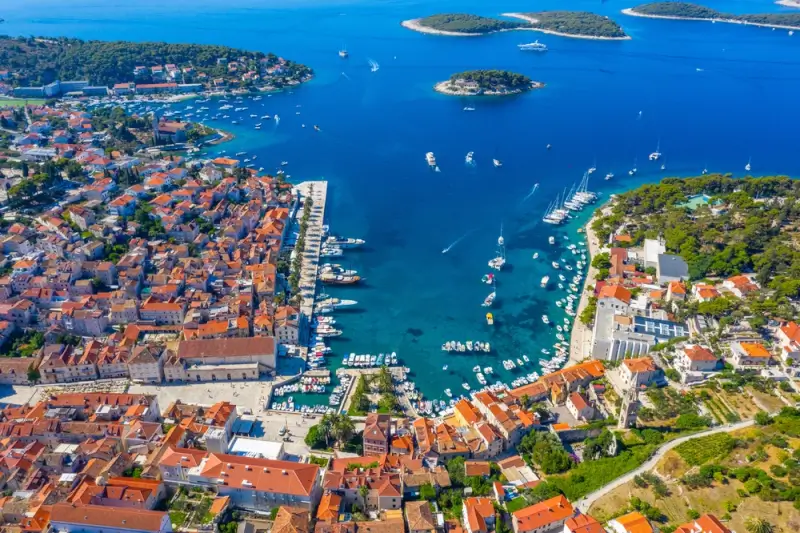 Aerial view of Hvar Town harbor with red-roofed buildings, yacht-filled marina, and Pakleni Islands in turquoise Adriatic waters