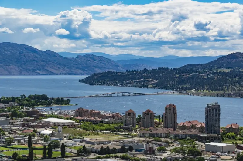 Aerial view of Okanagan Lake surrounded by mountains and downtown Kelowna cityscape with bridge connecting waterfront communities