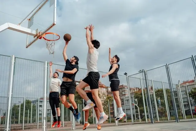 Group of players competing for rebound on public outdoor basketball court in urban neighborhood