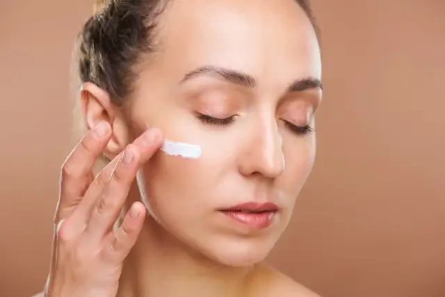 Woman applying white cream to her face with eyes closed demonstrating anti aging tips for youthful skin