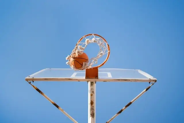 Basketball swishing through net on outdoor court hoop against clear blue sky