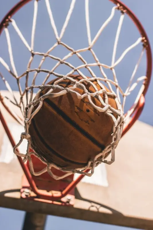 Close-up view of basketball dropping through hoop net from below on sunny day