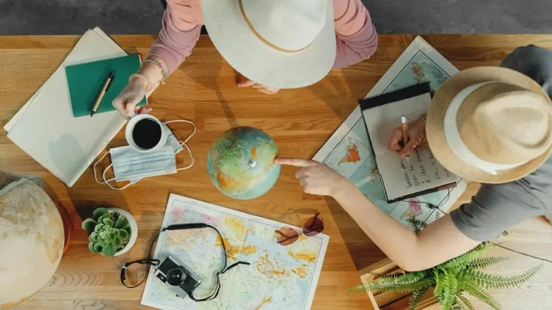 Couple planning bespoke travel itinerary with maps, globe, and notebooks on wooden table