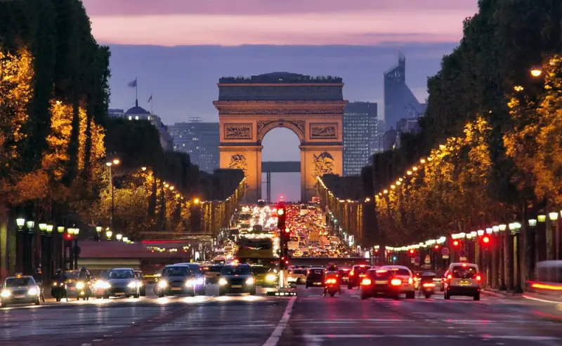 Arc de Triomphe illuminated at dusk with traffic flowing along the Champs-Élysées in Paris, France