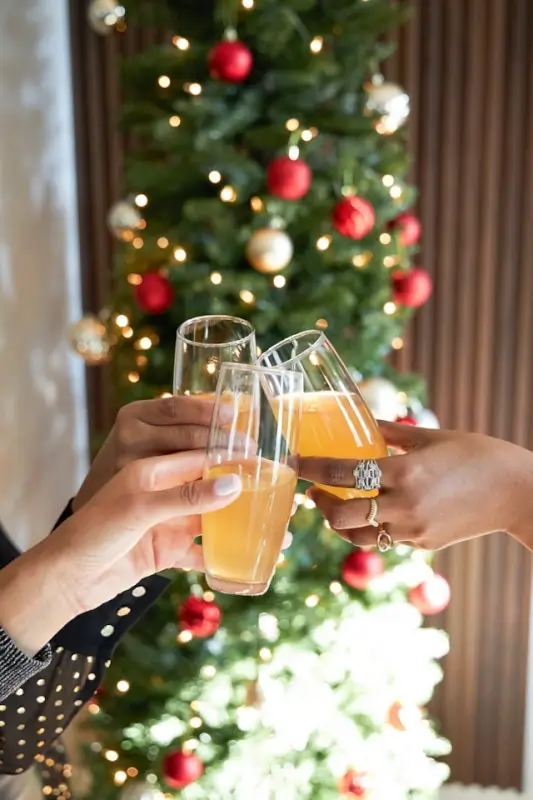 Three people clinking glasses filled with a festive drink in front of a decorated Christmas tree with red and gold ornaments.