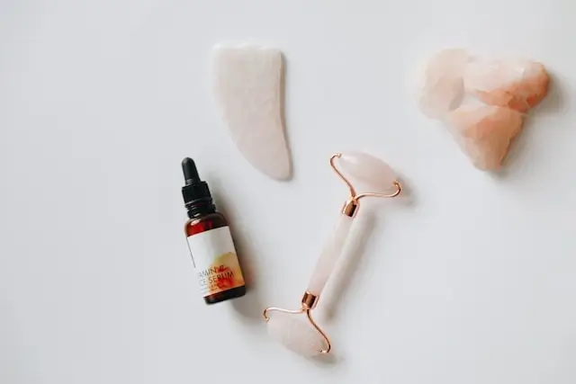 Facial serum bottle with rose quartz gua sha tools and jade roller on white background for skincare routine