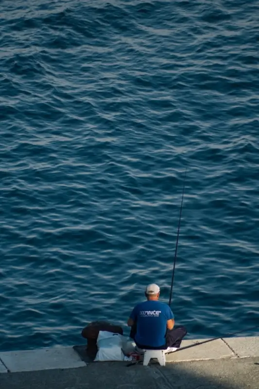 Angler wearing branded blue fishing shirt with logo casting line from pier into deep ocean waters