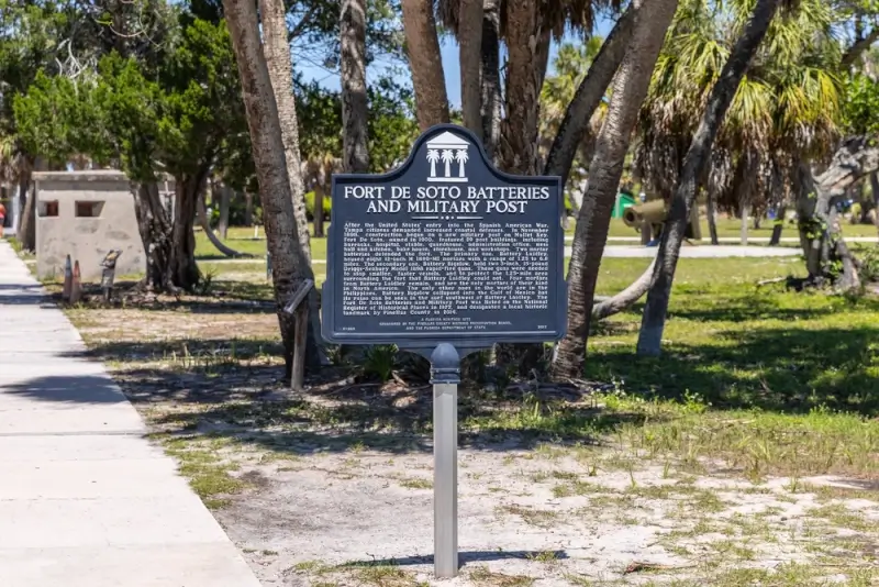 Fort De Soto Batteries and Military Post historical marker surrounded by palm trees at a Florida Gulf Coast park