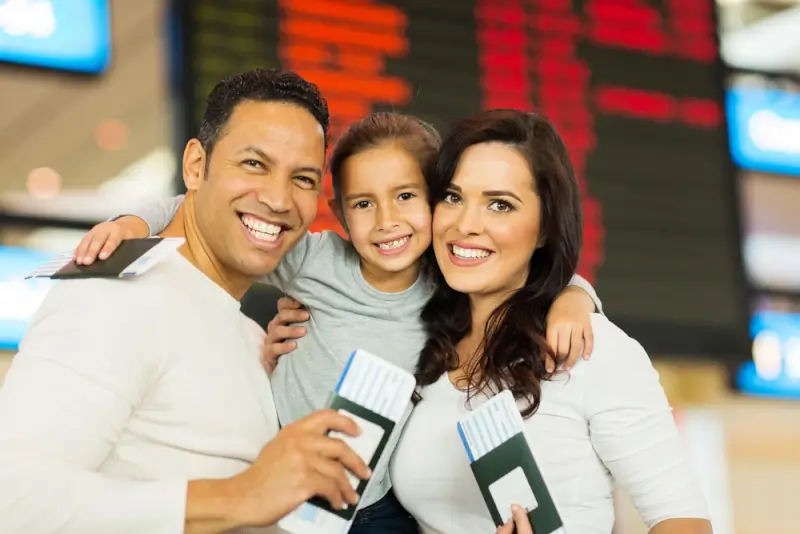 A happy family holding passports and boarding passes while standing together at an airport before moving abroad.