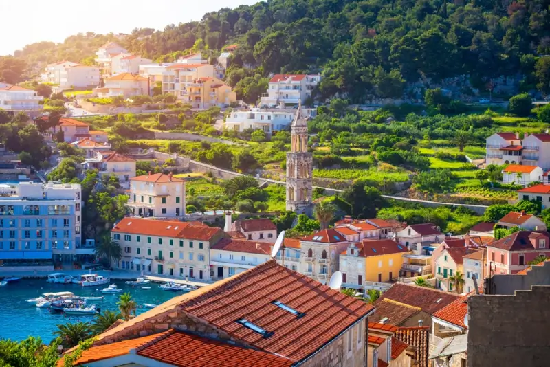 Hvar Town's historic waterfront with colorful buildings, church bell tower, and terraced hillside at golden hour