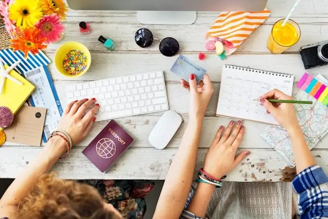 Overhead view of travelers planning vacation with passport, calendar, and map on desk, organizing holiday time wisely