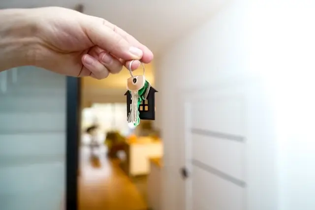 Hand holding house keys with home-shaped keychain for securing property before traveling