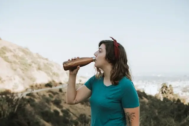 Woman staying hydrated with reusable water bottle during coastal hiking adventure