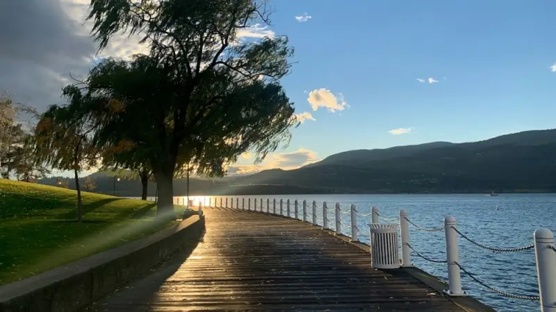Sunset view along Kelowna waterfront boardwalk with mountains reflecting on calm Okanagan Lake waters