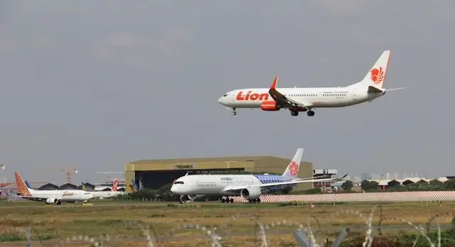 Commercial airplane approaching runway for landing at busy airport with multiple aircraft on tarmac