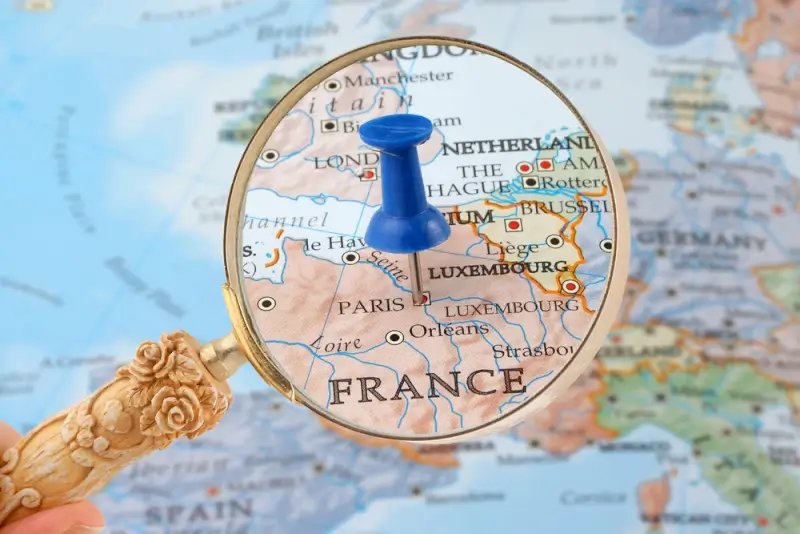 Magnifying glass focusing on Paris and central French regions on a European map with blue pushpin