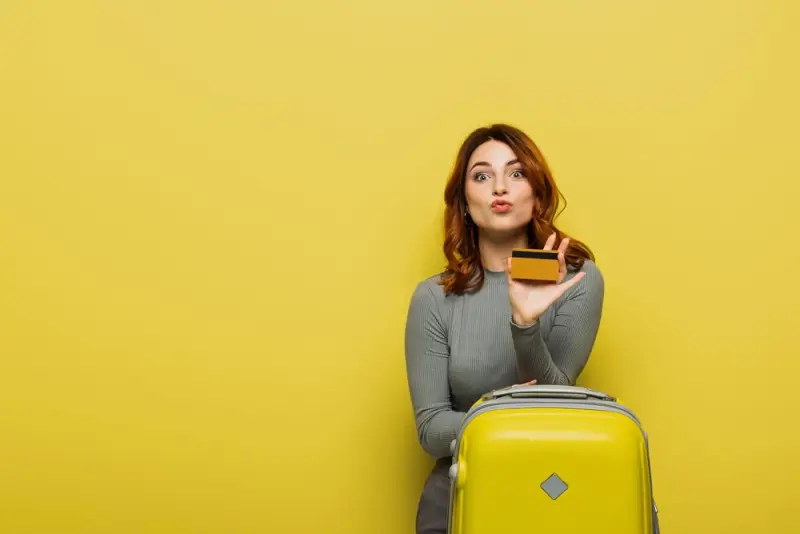 Money-savvy traveler holding credit card with yellow luggage for budget-friendly vacation planning