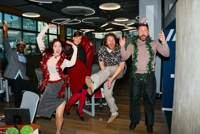 oworkers jumping in excitement while wearing holiday decorations and festive outfits at an office Christmas party.
