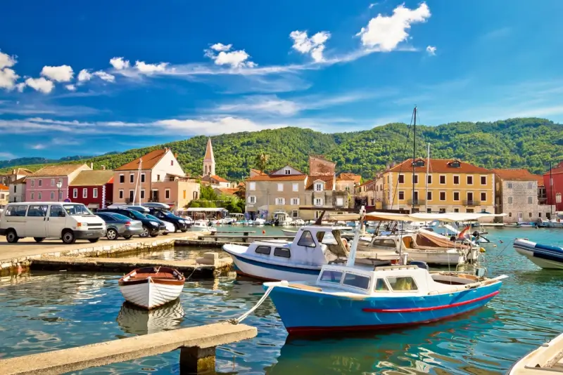 Traditional fishing boats moored in Stari Grad's old harbor with colorful Mediterranean buildings and green hills behind