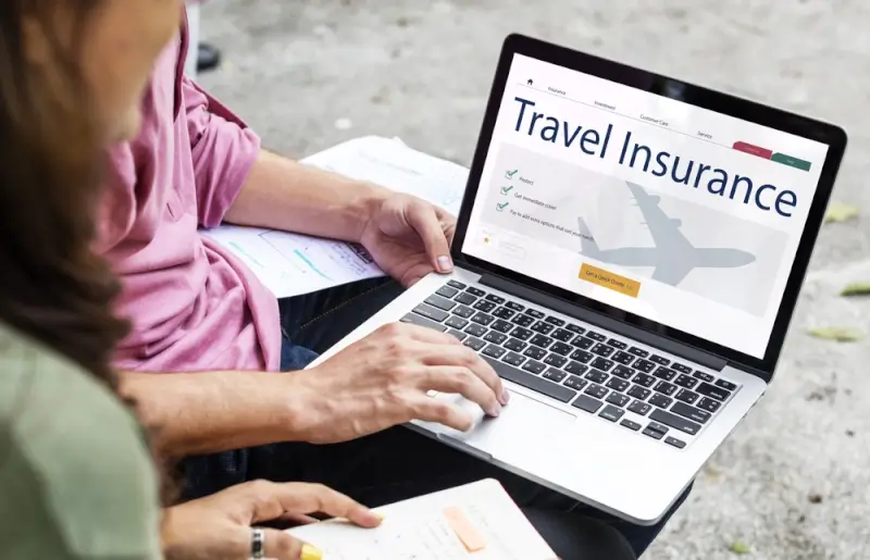 A person browsing travel insurance options on a laptop, comparing plans and coverage details online before an international trip.