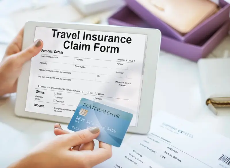 A person holding a tablet with a travel insurance claim form displayed, along with a credit card and paperwork for filing a claim after an overseas incident.