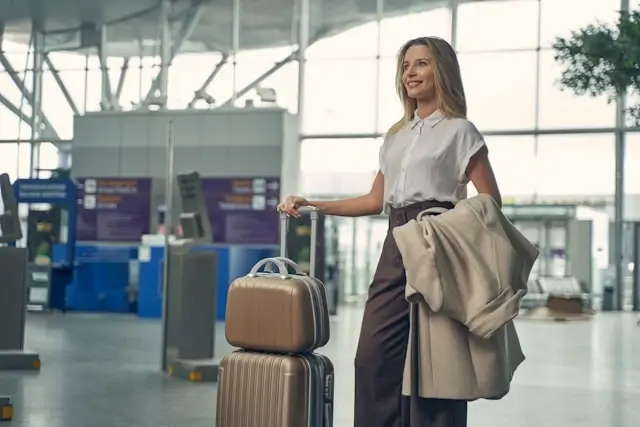 Woman walking through airport terminal with beige rolling suitcase and travel bag prepared for safe international travel