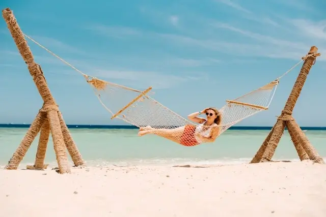 Woman relaxing in hammock on tropical beach with turquoise water, living a fulfilling lifestyle through frequent travel