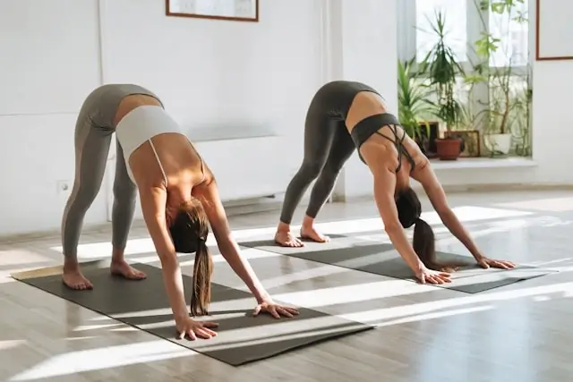 Two women practicing downward dog pose in yoga class for mental and physical wellness
